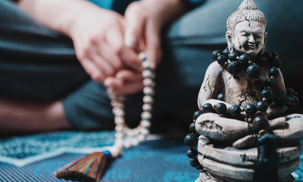 small buddha statue and blurry person behind holding mala